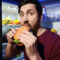 Man eating burger near refrigerator in kitchen at night Bad habit